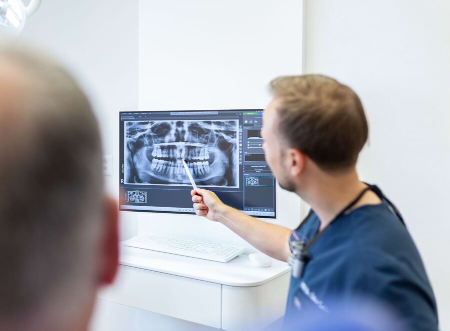 PD Dr. Silvio Valdec zeigt einem Patienten in der Beratung eine Aufnahme eines Kiefers.