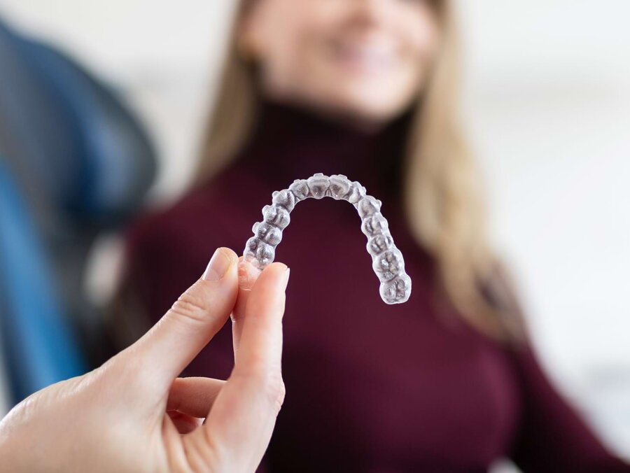 Nahaufnahme einer Aligner-Schiene. Im Hintergrund ist verschwommen eine Patientin zu sehen.